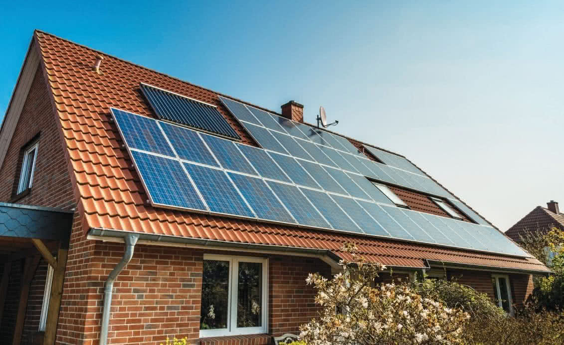 Rurowy kolektor słoneczny wśród kilkunastu paneli fotowoltaicznych na części połaci dachu spadzistego domu. fot. BDR Thermea Poland